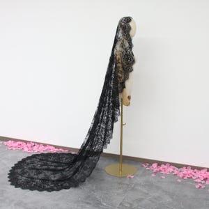 May include: A long black lace veil with a scalloped edge. The veil is draped over a mannequin and is displayed against a white background.