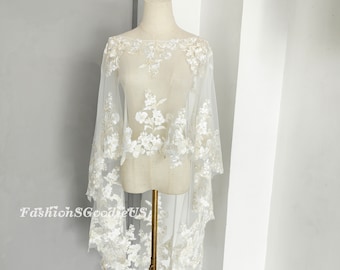 May include: White lace bridal cape with floral embroidery. The cape is sheer and has a scalloped edge.