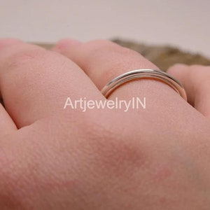 May include: A silver ring with a simple, polished design. The ring is worn on a person's finger.