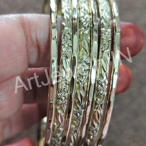 May include: Set of six gold-tone bangles with a floral design. The bangles are stacked on top of each other and have a hammered texture.