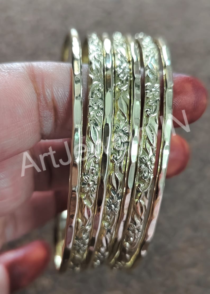 May include: Set of six gold-tone bangles with a floral design. The bangles are stacked on top of each other and have a hammered texture.