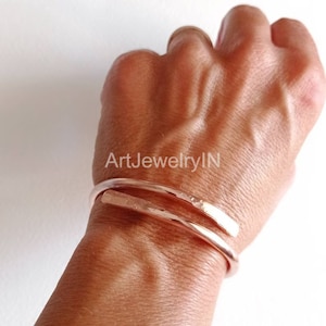 May include: A rose gold hammered metal cuff bracelet. The bracelet is made of two pieces of metal that are wrapped around the wrist. The bracelet is simple and elegant.