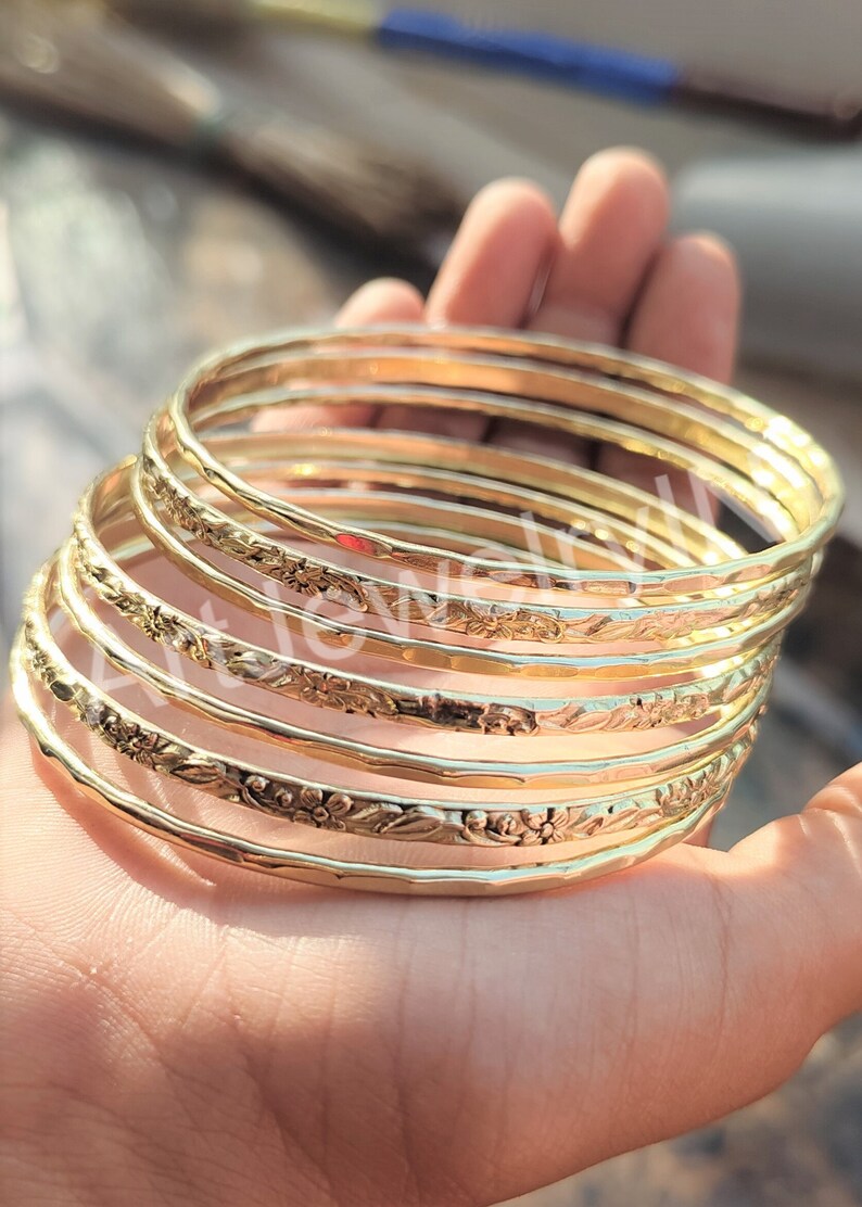 May include: A set of six gold-toned bangles with a floral design. The bangles are stacked on top of each other and have a hammered texture.