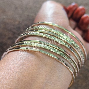 May include: A set of eight gold-toned bangles with an etched floral design. The bangles are stacked on a person's wrist.