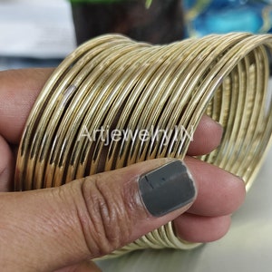 Peut inclure: Une pile de bracelets de couleur or. Les bracelets sont fins, ronds et semblent être en métal. L'image est un gros plan, montrant les détails des bijoux. Le texte "ArtjewelryIN" est visible.