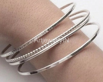 May include: A set of four silver bangles, one with a beaded design, worn on a wrist.