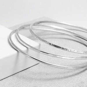 Può includere: Quattro braccialetti d'argento impilati uno sopra l'altro. I braccialetti sono lisci e lucidi.