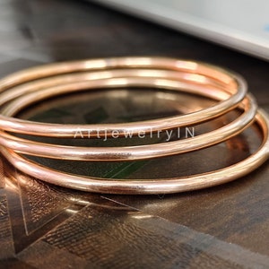 Op de afbeelding: Drie gouden armbanden die op elkaar gestapeld zijn. De armbanden zijn glad en glanzend.