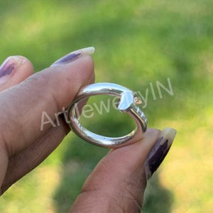 Puede incluir: Un anillo de plata con un diseño abierto único. El anillo está hecho de metal liso y pulido y tiene un aspecto simple y moderno.