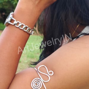 May include: Silver wire arm bracelet with a spiral design. The bracelet is worn on a person's upper arm.