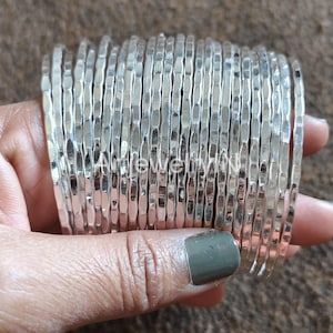May include: A stack of silver hammered metal bangles. The bangles are thin and have a textured surface.