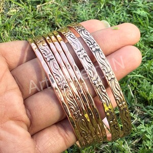 Peut inclure: Un ensemble de huit bracelets en cuivre avec un motif floral. Les bracelets sont empilés les uns sur les autres et ont une texture martelée.