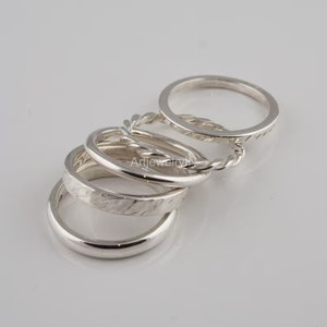 May include: A set of five silver stacking rings with different textures. The rings are stacked on top of each other, with the widest ring at the bottom and the narrowest ring at the top.