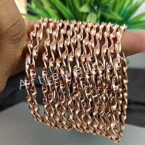 Peut inclure: Un ensemble de 12 bracelets dorés avec un design torsadé. Les bracelets sont empilés les uns sur les autres.