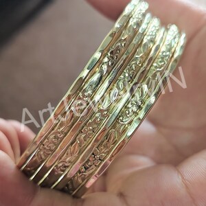 May include: A set of five gold-toned bangles with a floral design. The bangles are stacked on top of each other.