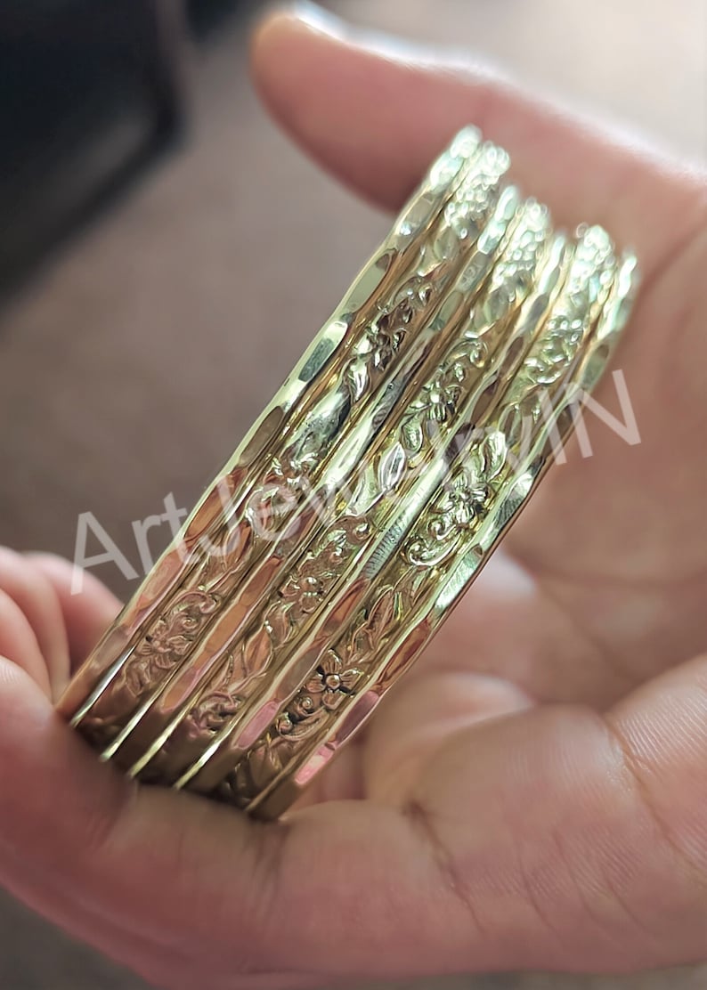 May include: A set of five gold-toned bangles with a floral design. The bangles are stacked on top of each other.
