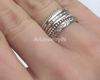 May include: A set of four silver stacking rings. The rings are all different styles, with one featuring a floral design, one with a beaded design, and two with textured bands.