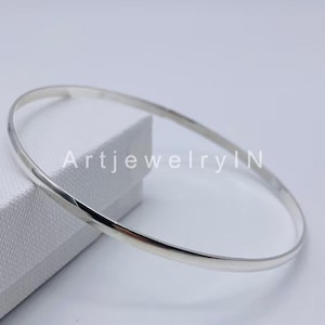 Puede incluir: Un brazalete de plata simple. El brazalete es liso y brillante, y es un estilo clásico que se puede usar con cualquier atuendo.
