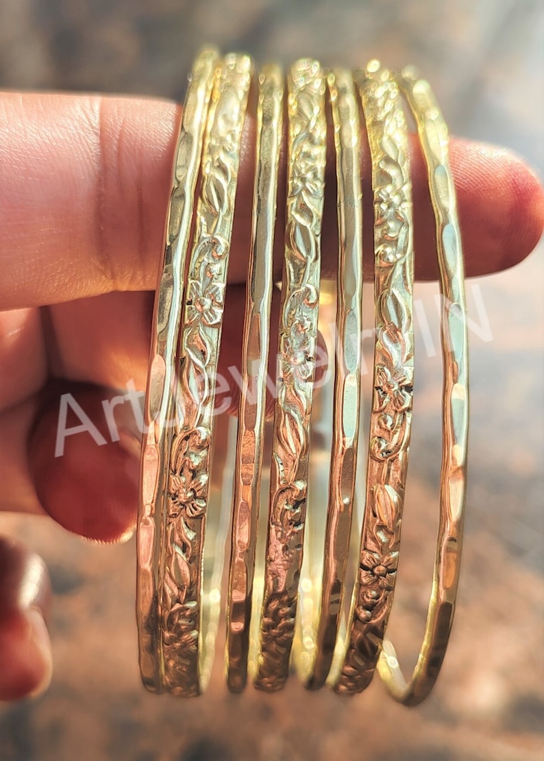 May include: A set of seven gold-toned metal bangles with a floral design. The bangles are stacked on top of each other and have a hammered texture.