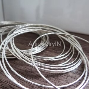 Peut inclure: Une pile de bracelets en métal argenté à la texture martelée. Les bracelets sont disposés en cercle, le bracelet du haut chevauchant partiellement les autres.