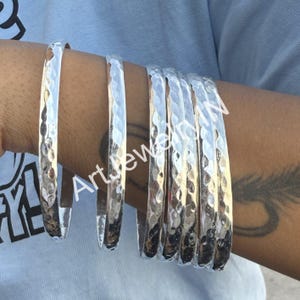 May include: Set of six silver hammered bangle bracelets. The bracelets are stacked on a person's wrist.