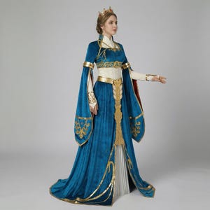 May include: A teal velvet gown with gold trim and accents. The dress features long, flowing sleeves, a high collar, and a gold crown. The bodice has gold embroidery, and the skirt flares out from the waist. The gown is a medieval or fantasy style.