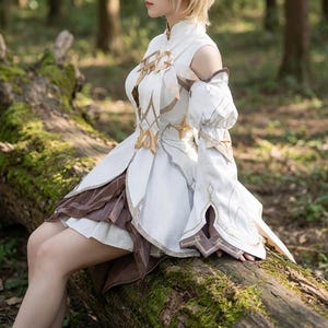 Puede incluir: Un vestido de cosplay blanco y marrón con detalles dorados. El vestido presenta un cuello alto, hombros descubiertos y mangas largas con estrellas doradas decorativas. La falda tiene tela marrón y blanca en capas. El vestido se usa al aire libre.