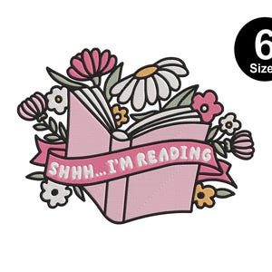 Puede incluir: Diseño de bordado rosa y blanco de un libro con flores y el texto "Shh... I'm reading".