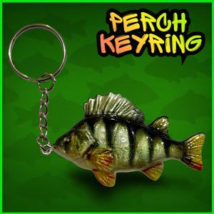 Peut inclure: Un porte-clés détaillé représentant un poisson perche. Le poisson est peint avec des couleurs réalistes, notamment des rayures jaunes, vertes et noires. Le porte-clés est doté d'un anneau et d'une chaîne de couleur argentée. Le texte "PERCH KEYRING" est affiché dans une police colorée.