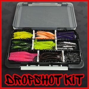 Puede incluir: Una caja de aparejos de plástico negro con tapa transparente, llena de varios señuelos de pesca coloridos. Los señuelos son en tonos de amarillo, naranja, verde, rosa, marrón y azul. El texto "DROPSHOT KIT" se muestra en rojo en la parte inferior.