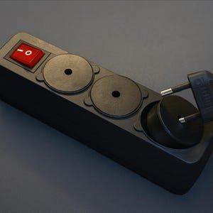 Op de afbeelding: Een zwarte stekkerdoos met drie stopcontacten en een rode aan/uit-schakelaar. Een zwarte stekker wordt in een van de stopcontacten gestoken. De stekkerdoos heeft een zwart snoer.