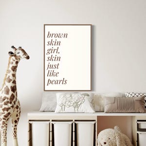 May include: A framed print with the text "brown skin girl, skin just like pearls" in brown lettering on a white background.