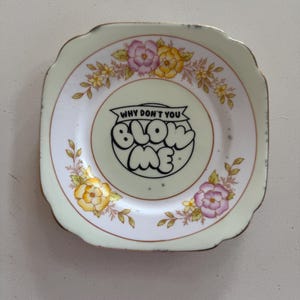 Può includere: Una tazza di ceramica bianca con manico nero e la scritta "But First, Coffee" in grassetto nero. La tazza è posta su uno sfondo sfocato, che suggerisce un'atmosfera accogliente.