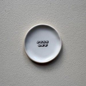 May include: White ceramic dish with a black inscription that reads "PISS OFF" in a retro font.