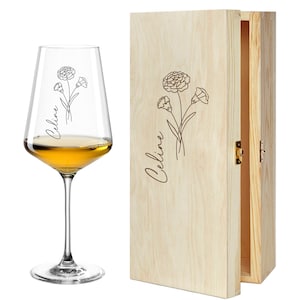 Könnte beinhalten: Ein Weinglas gefüllt mit bernsteinfarbener Flüssigkeit, neben einer hellen Weinkiste aus Holz. Sowohl das Glas als auch die Kiste weisen ein Blumendesign und den Namen "Celine" in Schreibschrift auf. Die Kiste ist geöffnet und zeigt ihr Inneres.