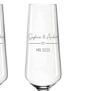 Puede incluir: Una flauta de champ&aacute;n transparente con los nombres "Sophia & Andre" en escritura elegante, un peque&ntilde;o coraz&oacute;n y la fecha "MAI 2023" impresa debajo. La cristaler&iacute;a est&aacute; dise&ntilde;ada para una boda o evento especial.