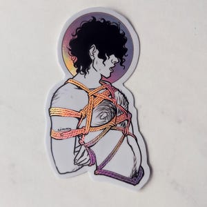 Puede incluir: Una pegatina con un dibujo lineal de una persona con el pelo rizado, atado con cuerdas de colores. El fondo es un degradado de rosa, morado y naranja.