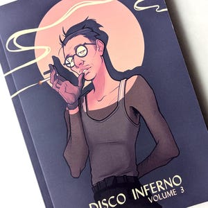 Peut inclure: Couverture de livre "DISCO INFERNO VOLUME 3" avec une illustration d'une personne fumant une cigarette, portant des lunettes et un débardeur. L'œuvre a un style de bande dessinée rétro avec un fond bleu foncé et un cercle rose-orangé.