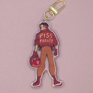 Könnte beinhalten: Ein Acryl-Schlüsselanhänger mit einer Comicfigur, die eine rote Jacke mit dem Text "PISS FAGGOT" auf dem Rücken trägt. Die Figur hält einen roten Helm in der linken Hand.