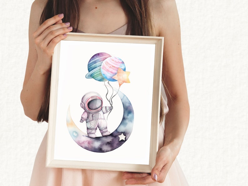 May include: Watercolor art print of an astronaut holding planet and star balloons while standing on a crescent moon. The artwork features a soft color palette of blues, purples, and pinks, perfect for a nursery or children's room.