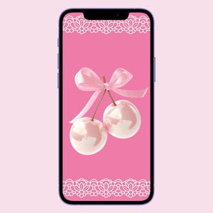 Könnte beinhalten: Ein rosa Smartphone mit rosa Hintergrund und einem weißen Spitzenrand. Der Bildschirm zeigt eine rosa Schleife, die um zwei rosa Kirschen gebunden ist.