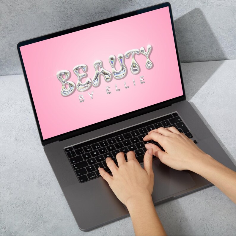 May include: A laptop computer with a pink screen displaying the text "BEAUTY BY ELLIE" in a silver, liquid-like font. The laptop is open and a person's hands are typing on the keyboard.