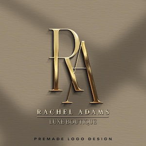 May include: Gold-coloured logo design featuring the letters "RA" in a stylised font. The text "RACHEL ADAMS LUXE BOUTIQUE" is below the logo, with "PREMADE LOGO DESIGN" at the bottom. The background is a neutral, textured brown.