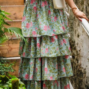 May include: A tiered skirt with a floral pattern in pink and green on a light blue background. The skirt is part of a two-piece outfit. The top is pink with a floral pattern. The outfit is suitable for summer wear.