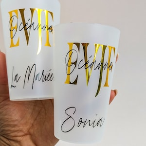 Może przedstawiać: Dwa białe plastikowe kubki z złotymi napisami "EVJF" i "Océanne" na jednym kubku i "La Mariée" na drugim kubku.