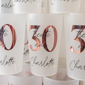 May include: A stack of white plastic cups with rose gold lettering. The cups are decorated with the name "Charlotte" and the number "30" with the text "trente ans" underneath.