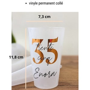 May include: A white plastic goblet with a gold vinyl design that says "trente cinq Enora" and the number 35. The goblet is 7.3 cm wide and 11.8 cm tall.