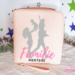 Könnte beinhalten: Eine rosa Reißverschlusstasche mit einer grauen Silhouette einer Familie mit zwei Erwachsenen und einem Kind. Der Text "Familie Mertens" ist in rosa Kursivschrift geschrieben.