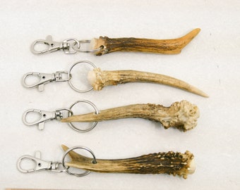 May include: Four antler keychains with silver key rings and clips. Each keychain features a different antler shape and size.