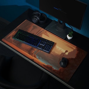 May include: A black keyboard with illuminated keys, a black mouse, and a headset sit on a large desk mat. The mat features a landscape design in shades of brown, orange, and blue. A computer monitor and a small potted plant are also visible.